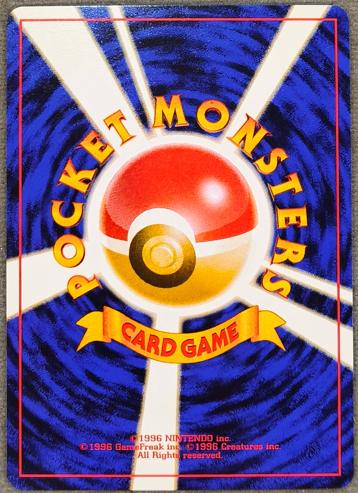 A vintage Pokémon Card Game booster pack sleeve featuring the classic blue and white design with a red and yellow Pokéball logo in the center, placed on a gray textured fabric background.