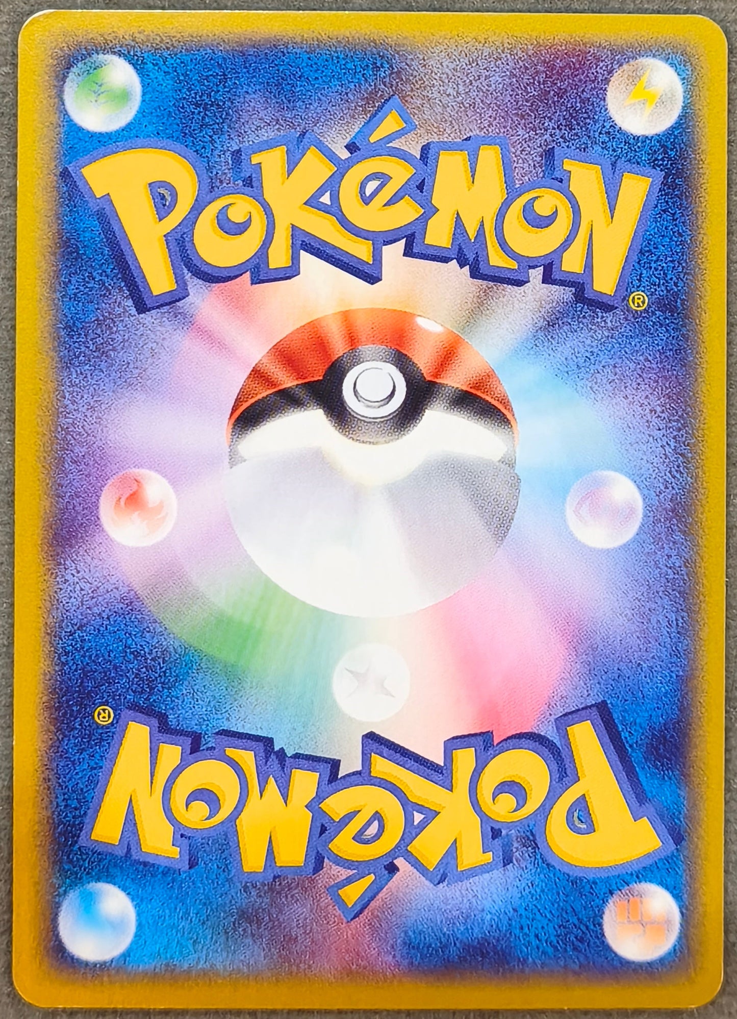 A Pokémon trading card with a blue and purple starburst background, a central Poké Ball graphic, and yellow 'Pokémon' logos at the top and bottom, photographed on a textured gray surface.